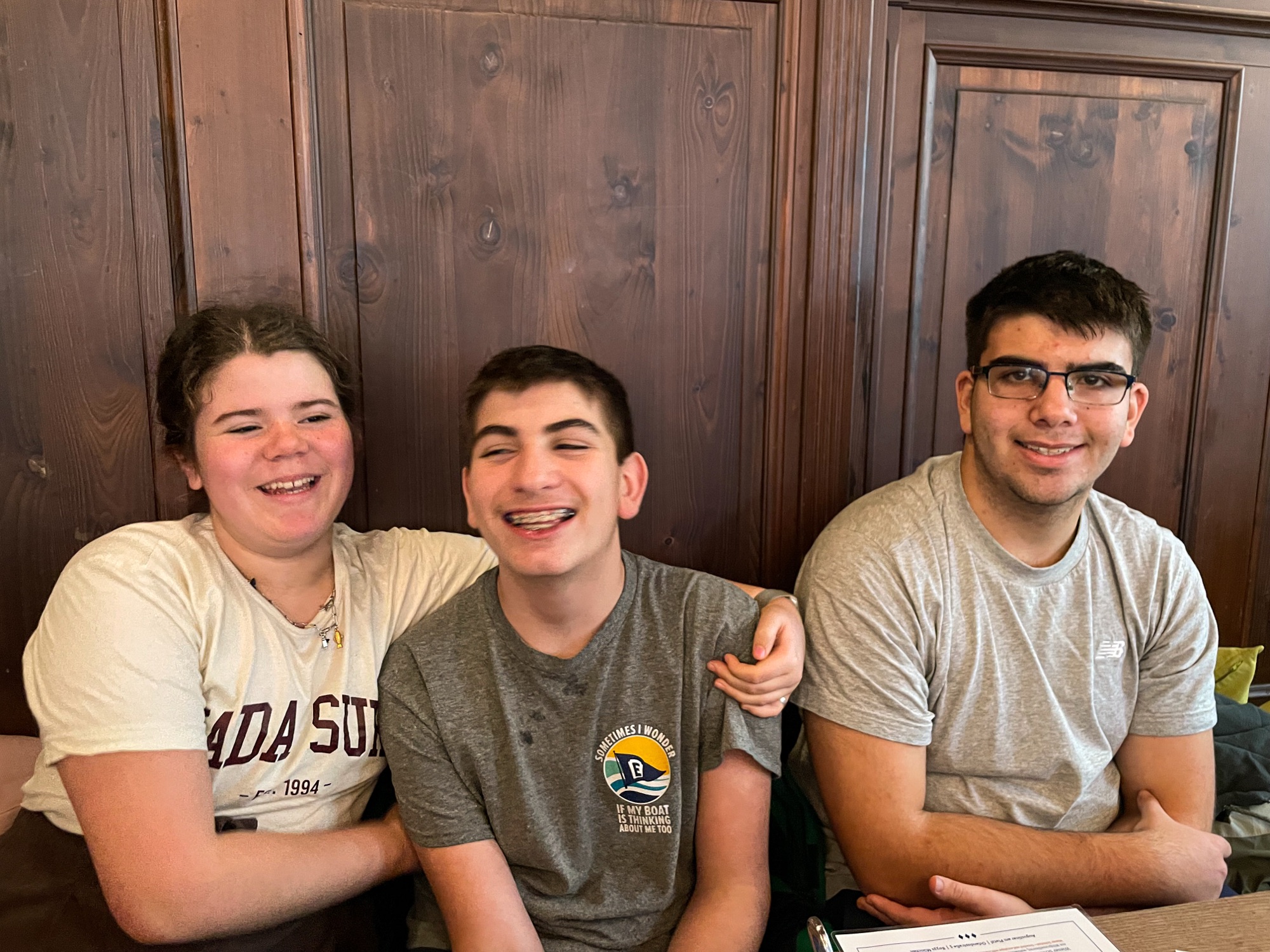 Three smiling young friends sit together, enjoying each other's company in a cozy setting. They are sharing a light moment.