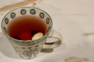 A decorative cup filled with glögg, a spiced mulled wine, sits on a marble surface, showcasing a slice of fruit and a nut. The intricate design of the cup adds a festive touch to the scene.