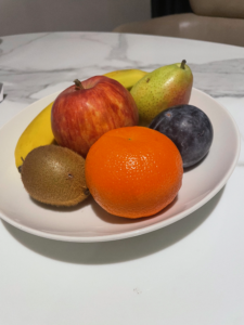 a bowl of fruit: an orange, plum, apple, kiwi and banana