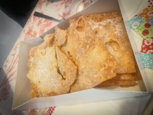 A box filled with crispy bugnes lyonnaises, a traditional pastry for Mardi Gras, dusted with powdered sugar. The pastries are arranged neatly, showcasing their delicate texture and golden color.