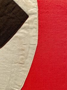 A close-up of a nazi flag with a red background and a black and white emblem partially visible. The texture of the material is evident.