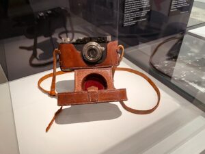 A vintage camera with a leather case and strap displayed at the Musée de la Liberation, highlighting the exhibit on war photographer Robert Capa.