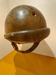 A worn military helmet with a dent from a bullet, displayed against a plain background. 