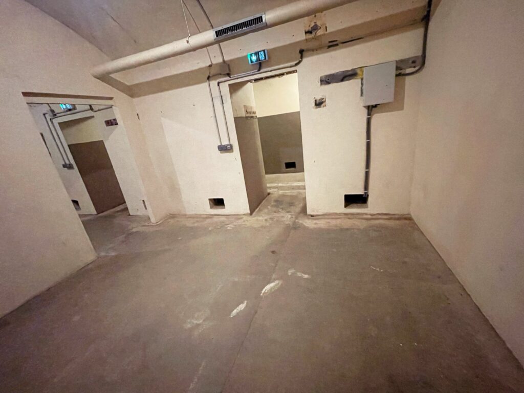 Empty interior space with bare walls, concrete floor, and exposed pipes. The area is unfinished and lacks any furnishings or decorations.