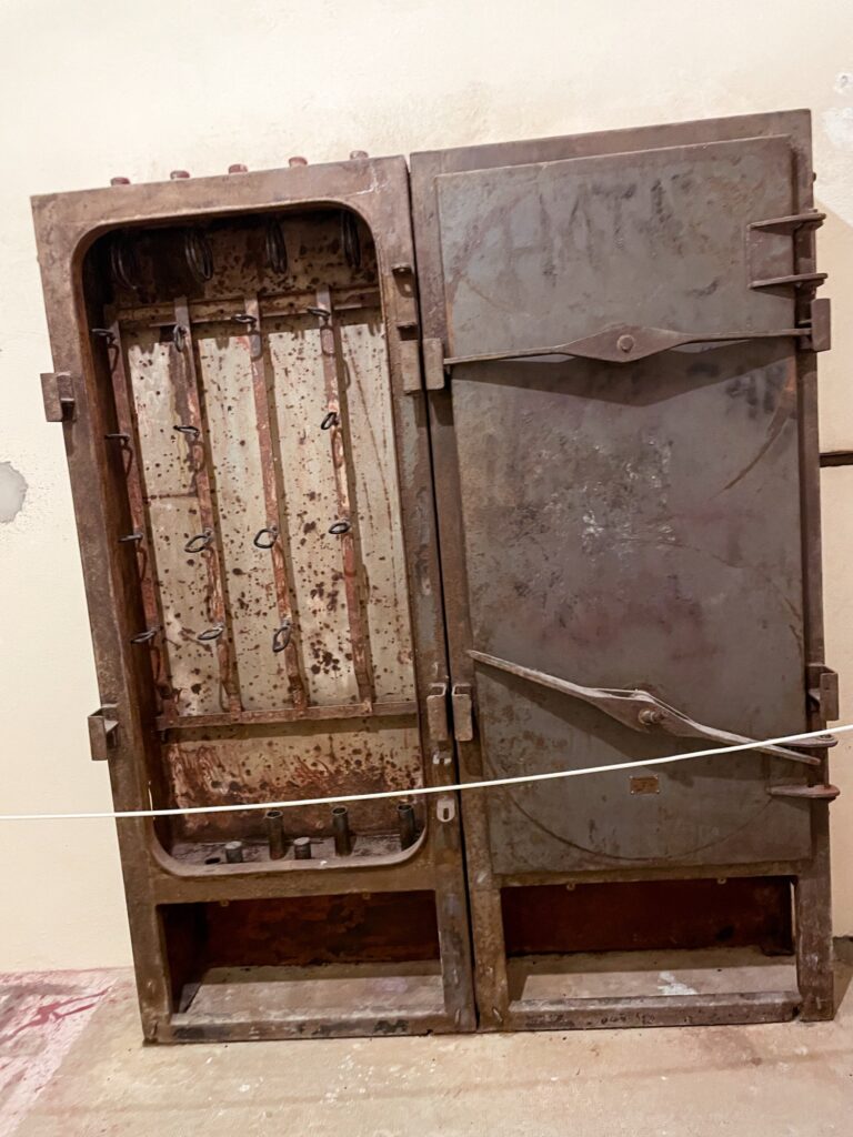 A rusty, old metal cabinet with a double door, featuring visible wear and tear, displayed in a museum setting.