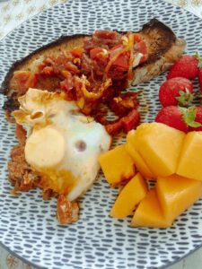 A plate of food featuring shakshouka, toast, fresh strawberries, and diced cantaloupe.
