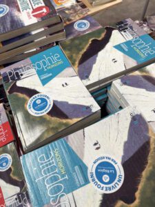 Stacks of philosophy textbooks are arranged in piles, showcasing their colorful covers and barcode stickers. The scene reflects a book return process at a school or library.